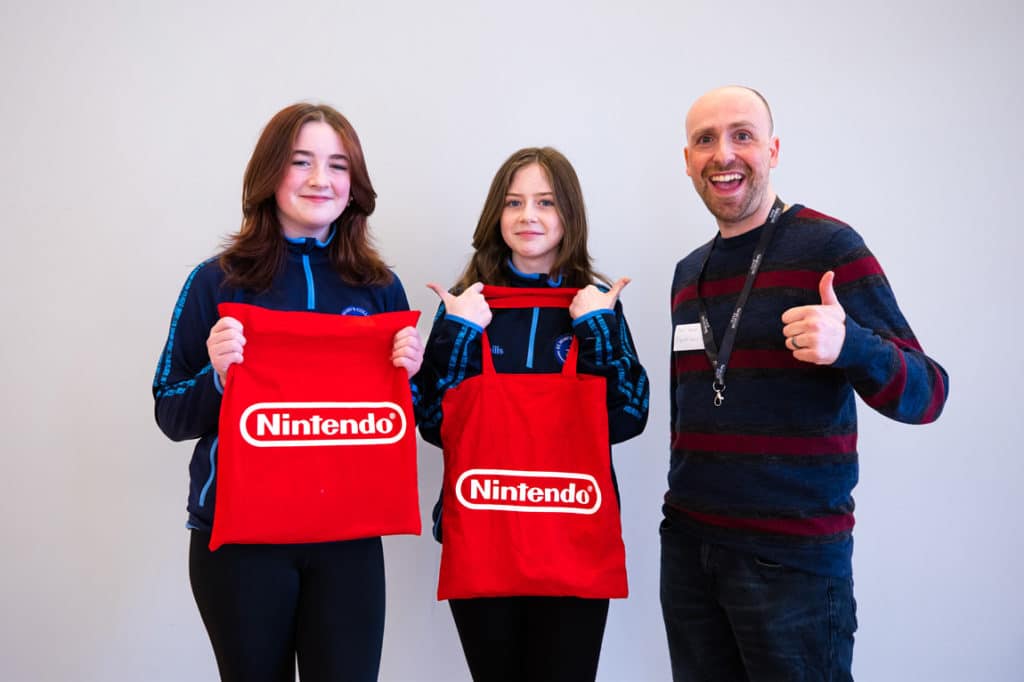 Erin Campbell and Orlaith Henry from St. Mary's College in Derry pose beside Esports News UK editor Dom Sacco for a Digital Schoolhouse journalism competition