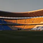 Floodlit stadium at golden hour with contrasting blue and gold atmospheric lighting.