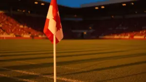 Empty floodlit football stadium at golden hour with dramatic shadow patterns on pitch, no players visible.